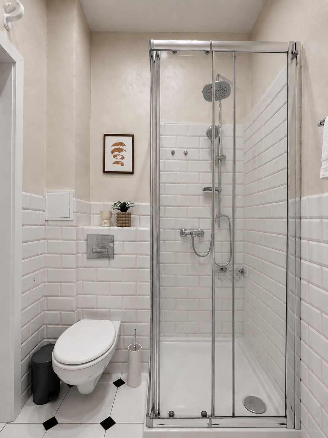 A modern bathroom with a glass-enclosed shower, white tiled walls, a toilet, and a small shelf with toiletries.