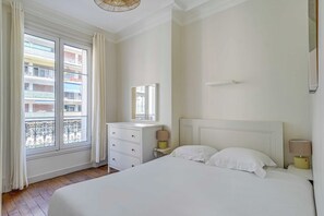 Un dormitorio con una cama grande, una mesita de noche, un aparador y una ventana con vistas al balcón.