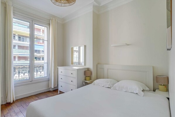 A bedroom with a large bed, a nightstand, a dresser, and a window with a balcony view. - 2BDR/4P apartment near Batignolles (Paris)
