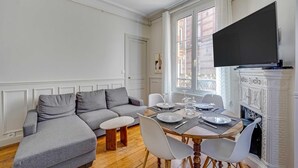 A living room with a grey sofa, a dining table set with plates and glasses, and a fireplace. - 2BDR/4P apartment near Batignolles (Paris)