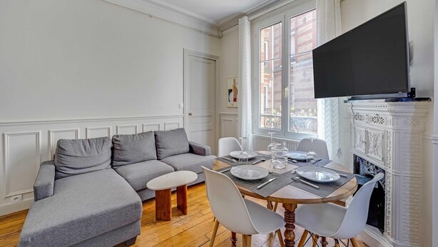 Een woonkamer met een grijze bank, een eettafel gedekt met borden en glazen, en een open haard.