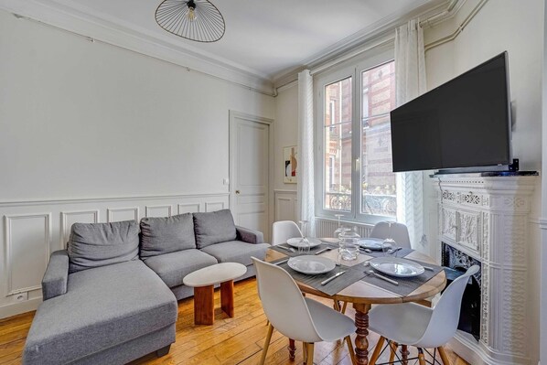 Una sala de estar con un sofá gris, una mesa de comedor con platos y vasos, y una chimenea.