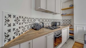 A kitchen with a wooden countertop, white cabinets, a built-in oven, and a backsplash with black and white tiles. - 2BDR/4P apartment near Batignolles (Paris)