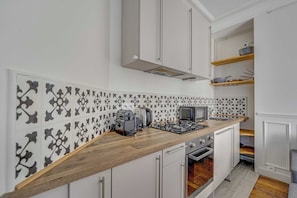 A kitchen with a wooden countertop, white cabinets, a built-in oven, and a backsplash with black and white tiles. - 2BDR/4P apartment near Batignolles (Paris)