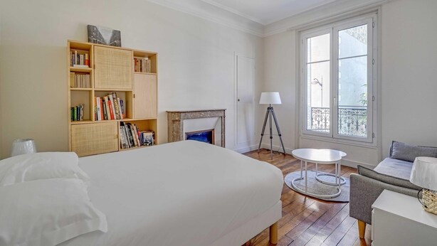 A bedroom with a bed, a bookshelf, a fireplace, a balcony with a railing, and a small round table. - 2BDR/4P apartment near Batignolles (Paris)