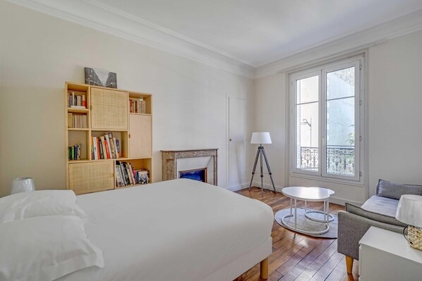 A bedroom with a bed, a bookshelf, a fireplace, a balcony with a railing, and a small round table. - 2BDR/4P apartment near Batignolles (Paris)