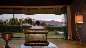 A person relaxing in a chair with a view of mountains through a glass door. - Kilimanjaro Luxury Camp (Moshi)