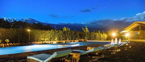 A nighttime resort pool area with lounge chairs, a pool, and a mountain in the background.