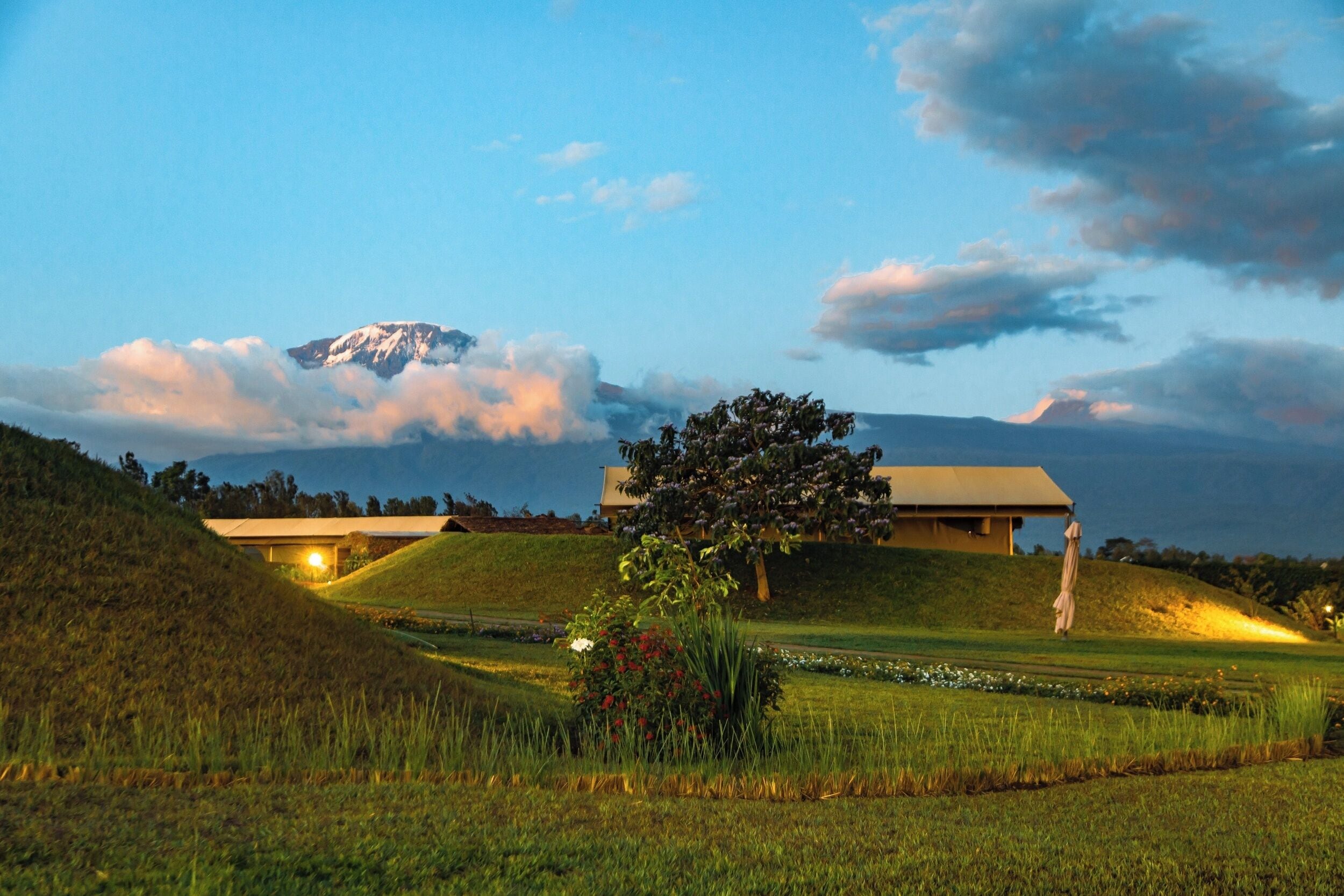 A building with a flat roof, surrounded by a grassy landscape, and a mountain in the background.