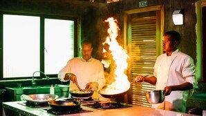 A kitchen with two chefs, one cooking with flames, and an exit sign. - Kilimanjaro Luxury Camp (Moshi)
