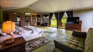 A bedroom with a bed, a TV, a sofa, and a view of the outdoors. - Kilimanjaro Luxury Camp (Moshi)
