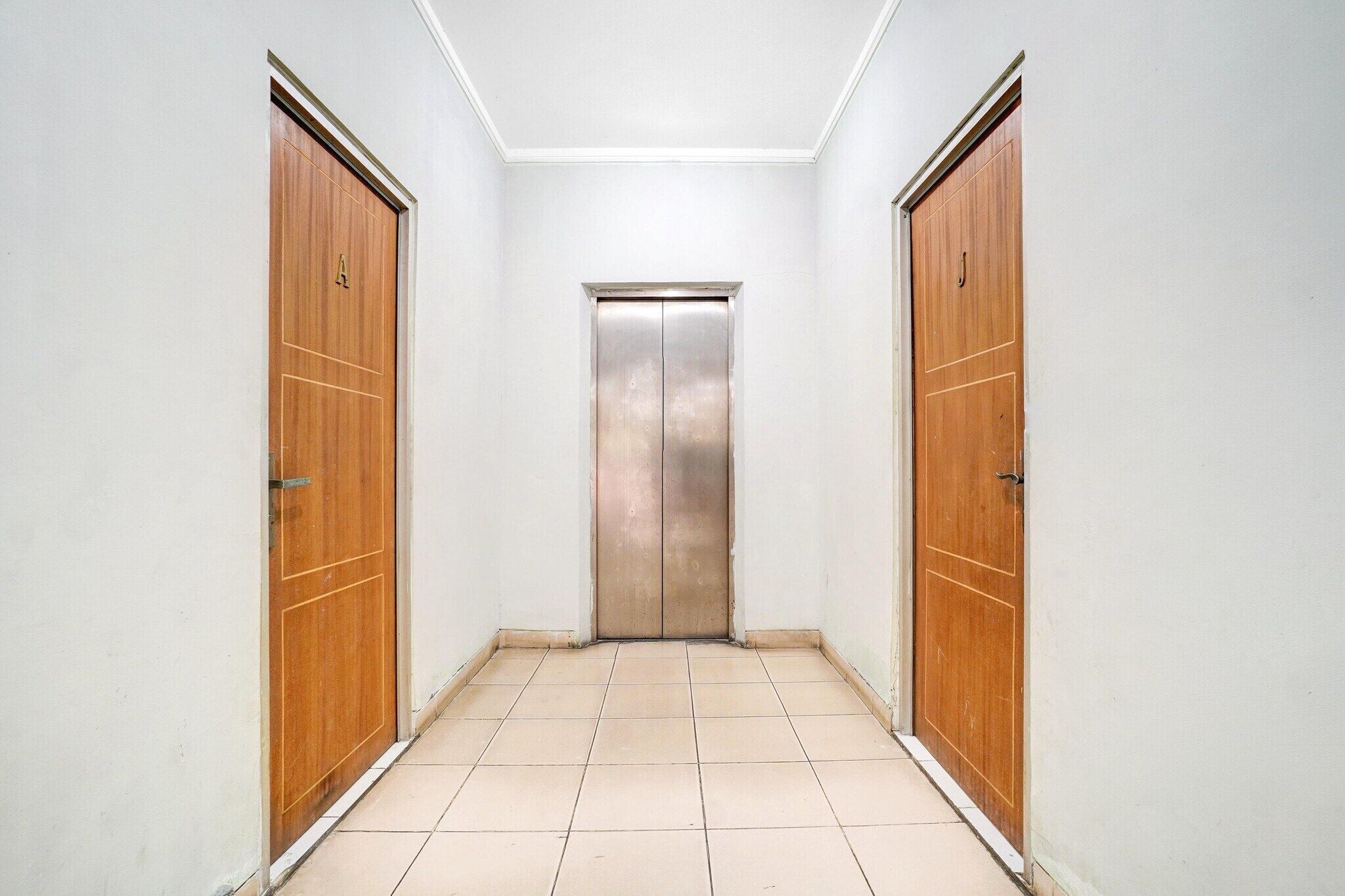 A hallway with two wooden doors and a central elevator.