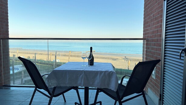 A balcony with a table and chairs, a bottle of wine, and a view of the beach and ocean. - Stylish Property With sea View (Jesolo)