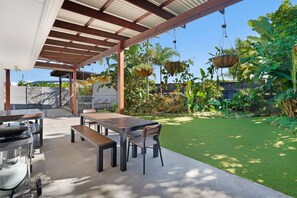 Eine Terrasse im Freien mit Tisch, Stühlen, einem Grill und hängenden Pflanzgefäßen.