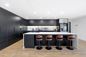 Eine moderne Küche mit dunklen Schränken, einer zentralen Kochinsel inklusive Barhocker und einem Edelstahlkühlschrank.