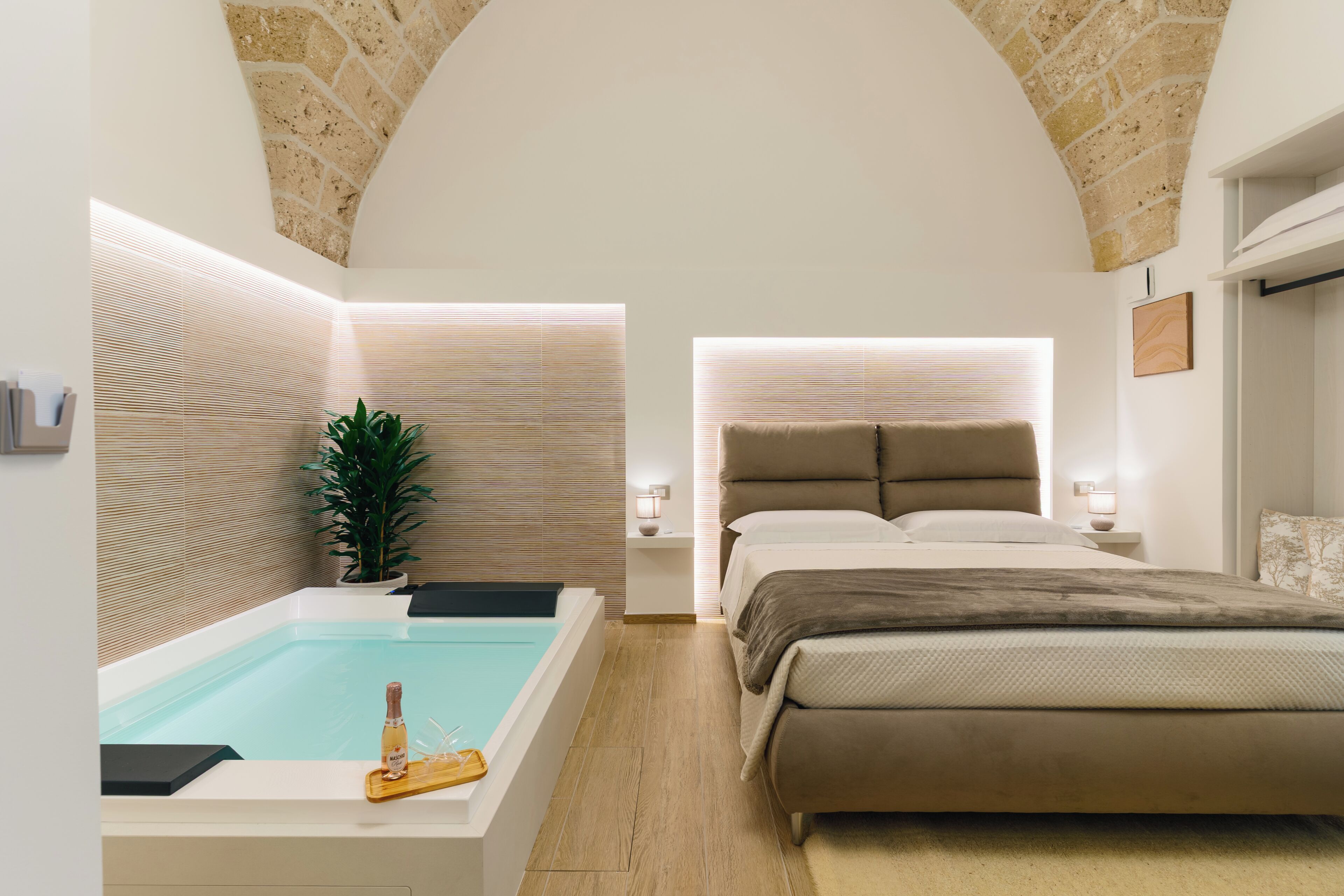A modern bedroom with a large bed, a built-in bathtub, and a potted plant.