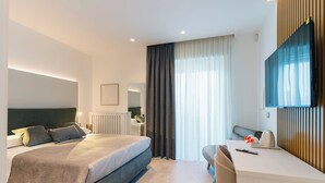 Ein modernes Hotelzimmer mit einem großen Bett, einem Schreibtisch, einem Sessel, einem Flachbildfernseher und einem Fenster mit Vorhängen.