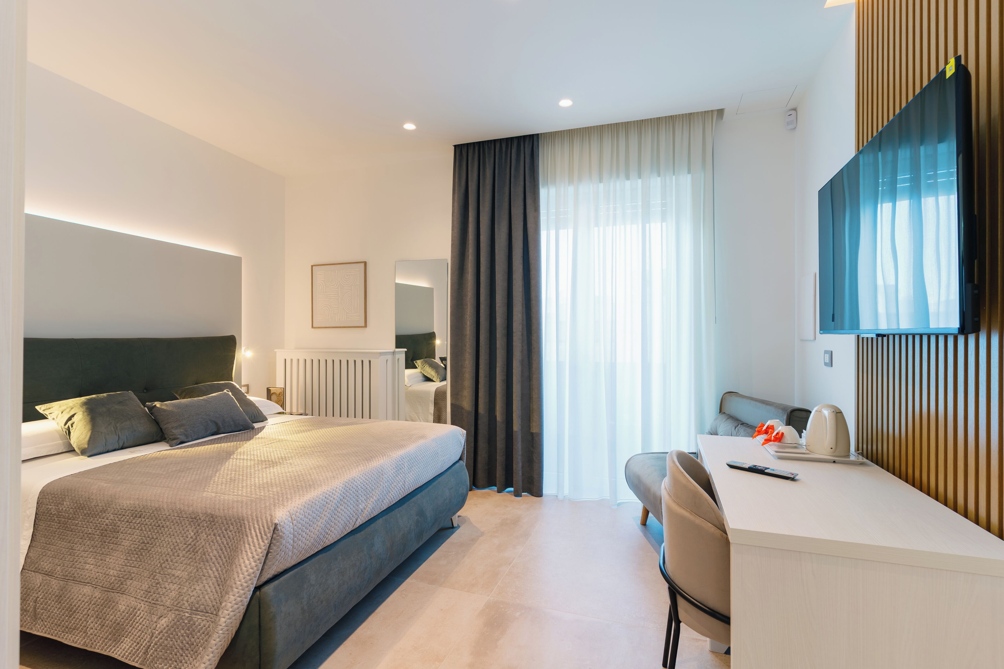 Una habitación de hotel moderna con una cama grande, un escritorio, una silla, un televisor de pantalla plana y una ventana con cortinas.