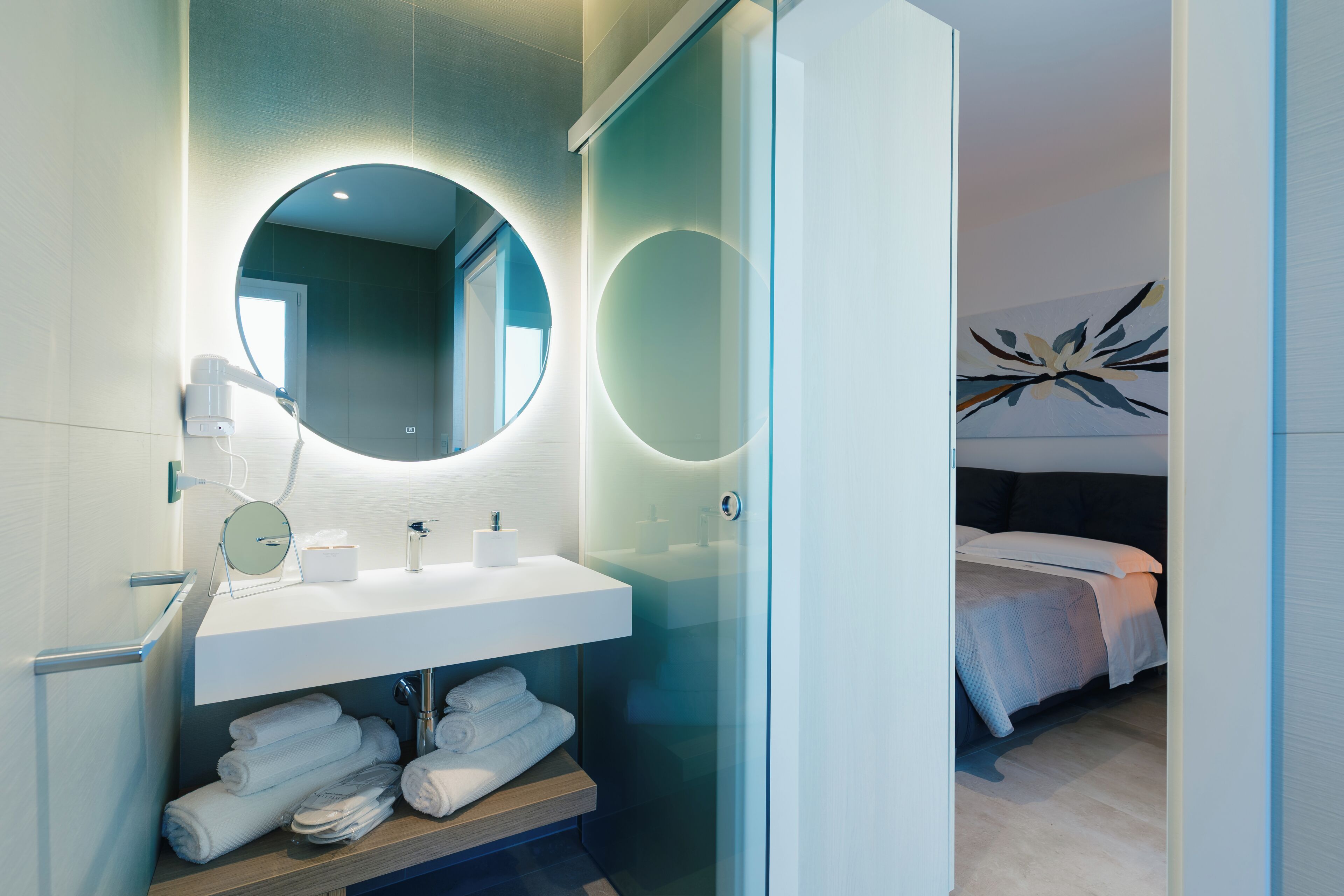 Ein modernes Badezimmer mit rundem Spiegel, weißem Waschbecken und ordentlich gefalteten Handtüchern.