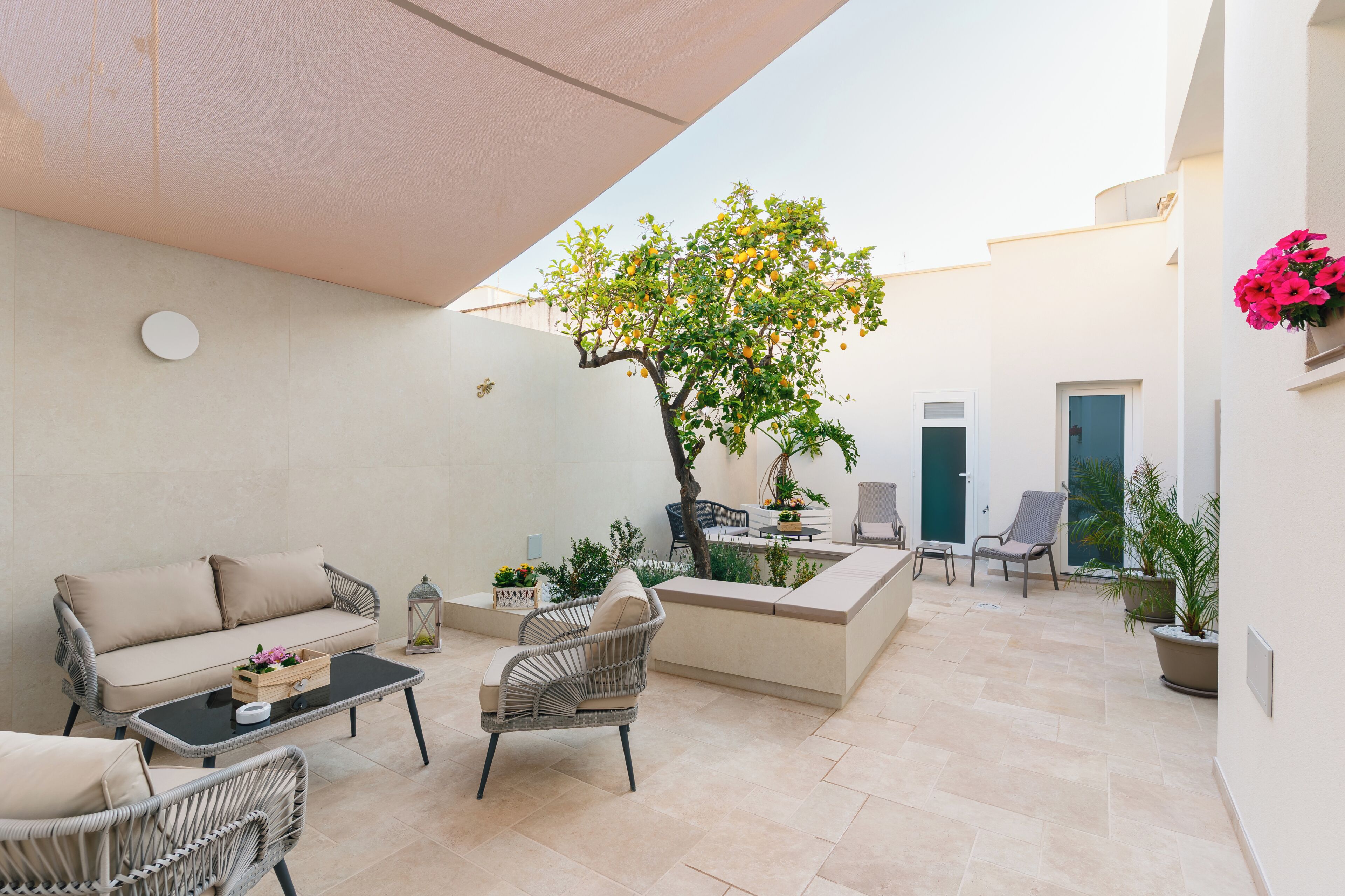 Un patio exterior con un sofá, sillas, una mesa, un árbol y plantas en macetas.