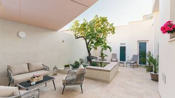 Un patio exterior con un sofá, sillas, una mesa, un árbol y plantas en macetas.