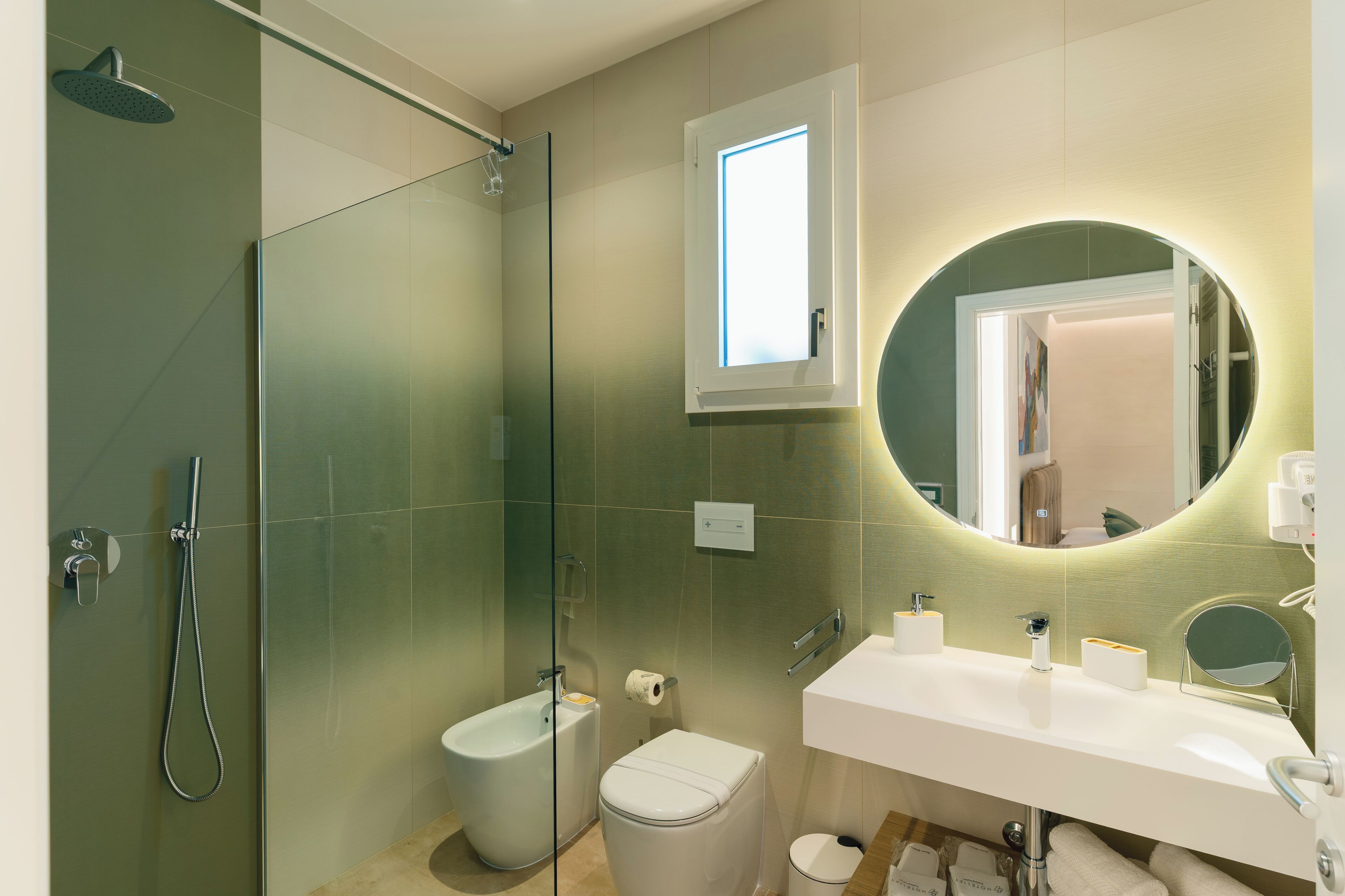 Un baño moderno con ducha de vidrio, inodoro, lavamanos con espejo y ventana sobre el espejo.