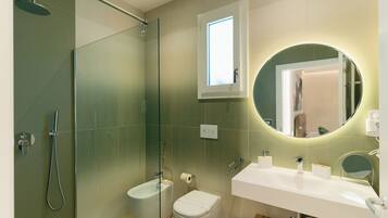 Un baño moderno con ducha de vidrio, inodoro, lavamanos con espejo y ventana sobre el espejo.