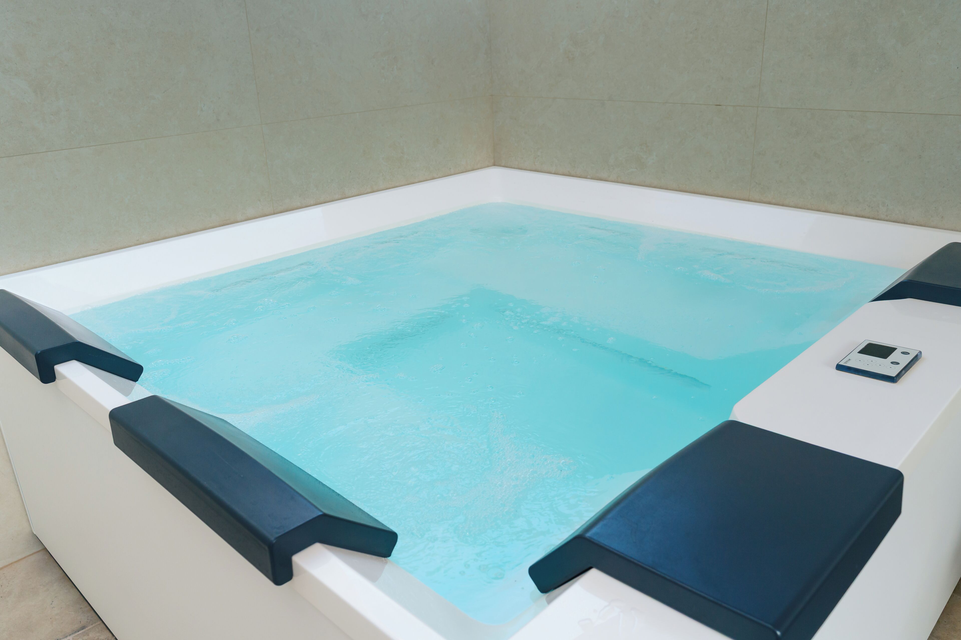 Una bañera moderna con un panel de control, rodeada por una pared de azulejos.