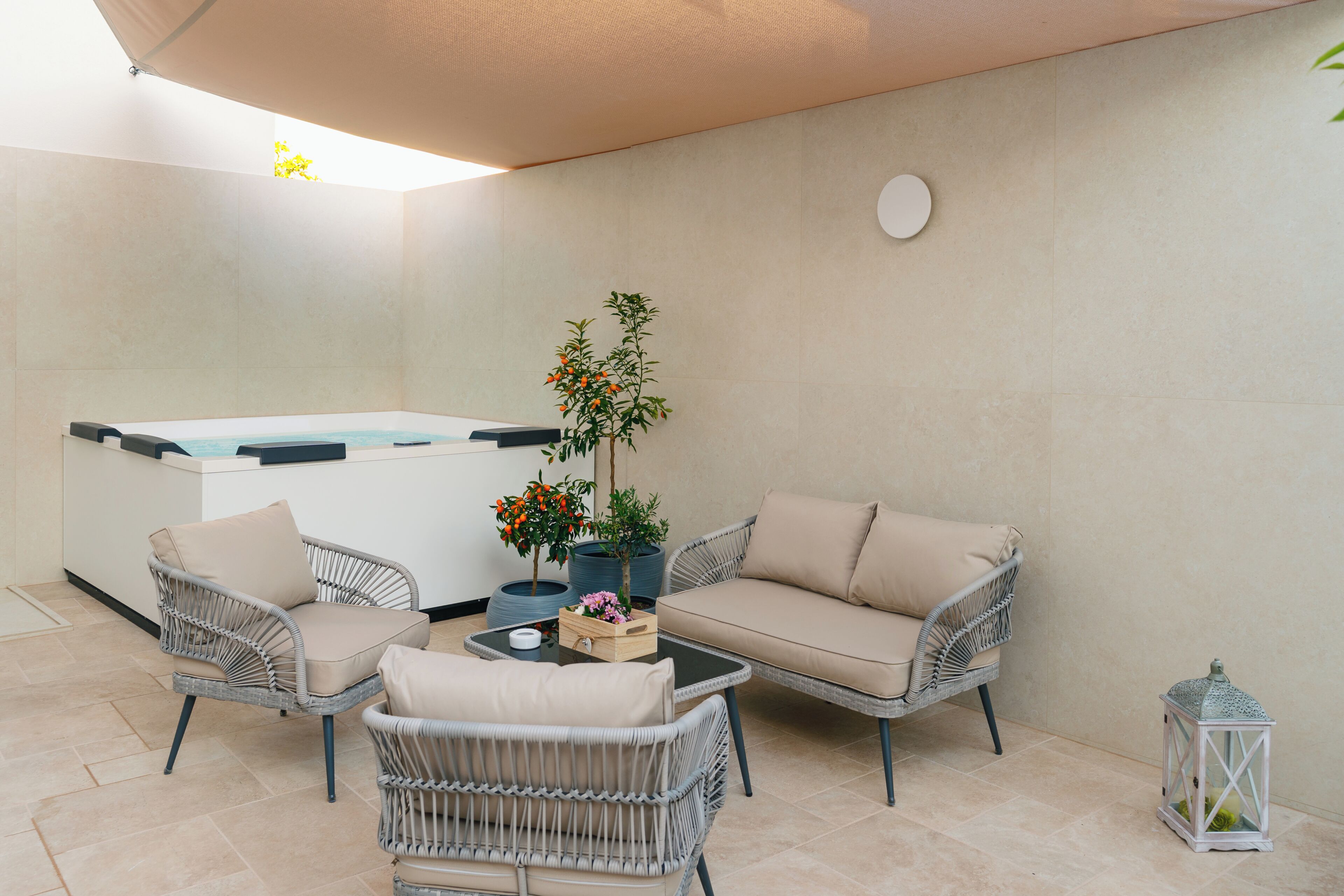 Un espacio patio con mobiliario de mimbre, un jacuzzi y plantas en macetas.