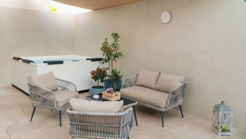 Un espacio patio con mobiliario de mimbre, un jacuzzi y plantas en macetas.