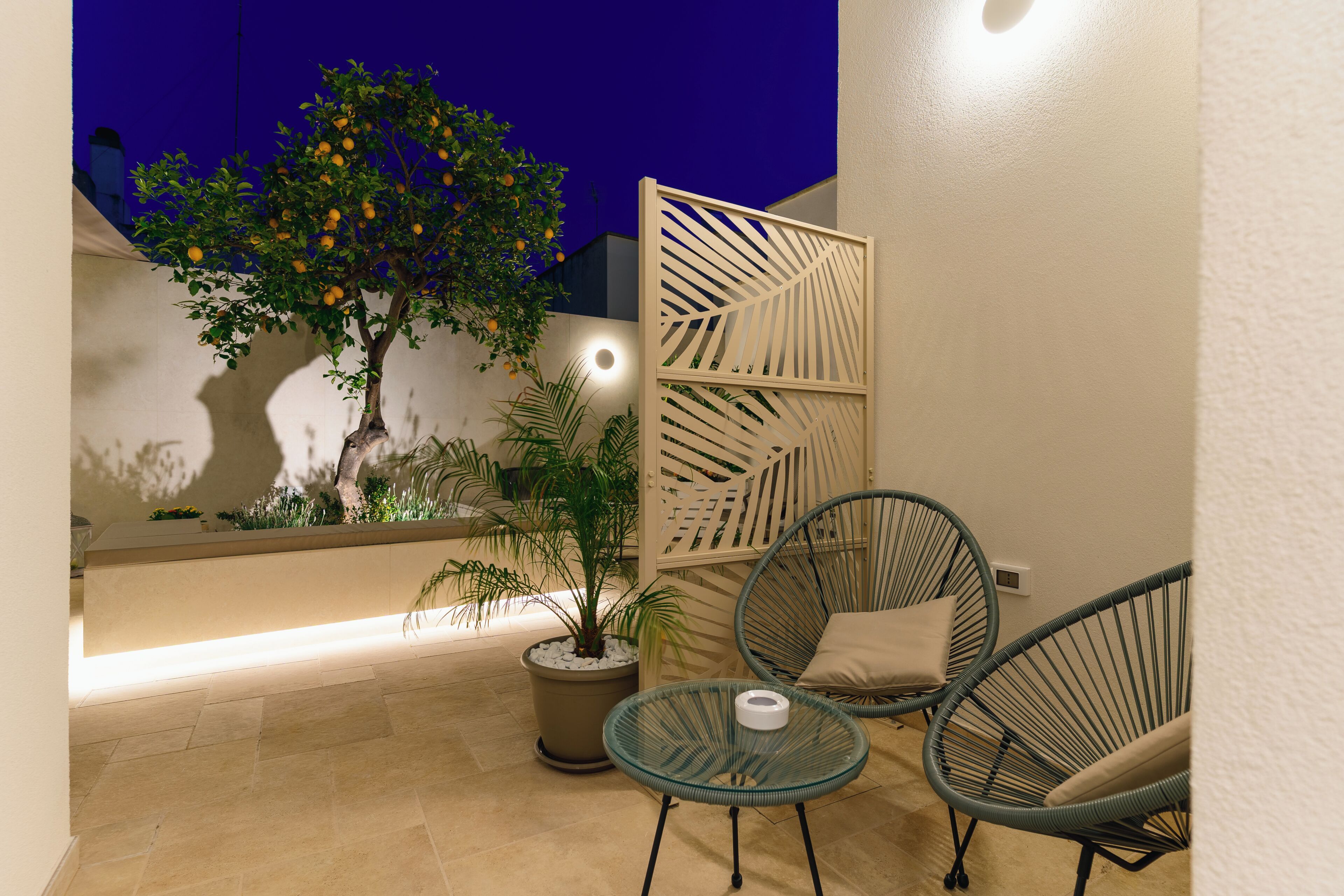 A patio with chairs, a potted plant, and a decorative screen.