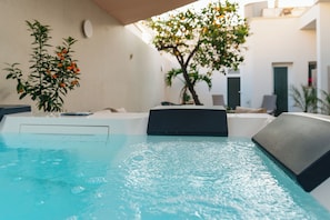 A pool area with a clear blue pool, a potted plant with orange flowers, and a modern building in the background. - B&B Palmares Rooms & Suites (Taviano)
