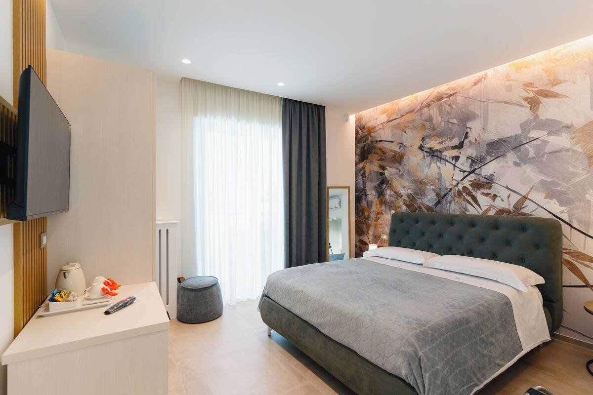 A modern hotel room with a large bed, a flat-screen TV, a bedside table, and a large abstract wall mural.
