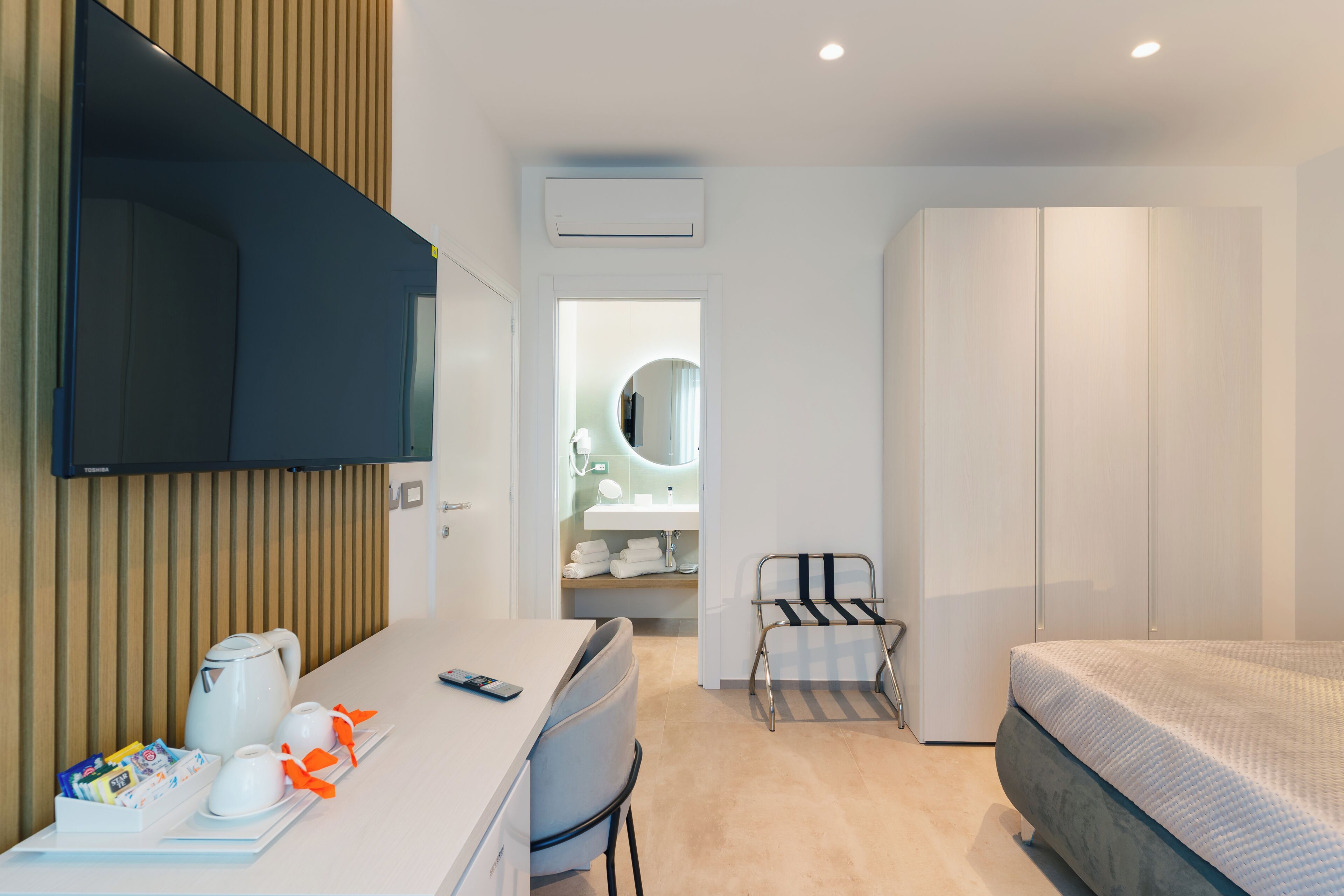 A modern hotel room with a desk, chair, bed, and a small seating area with a chair and table.