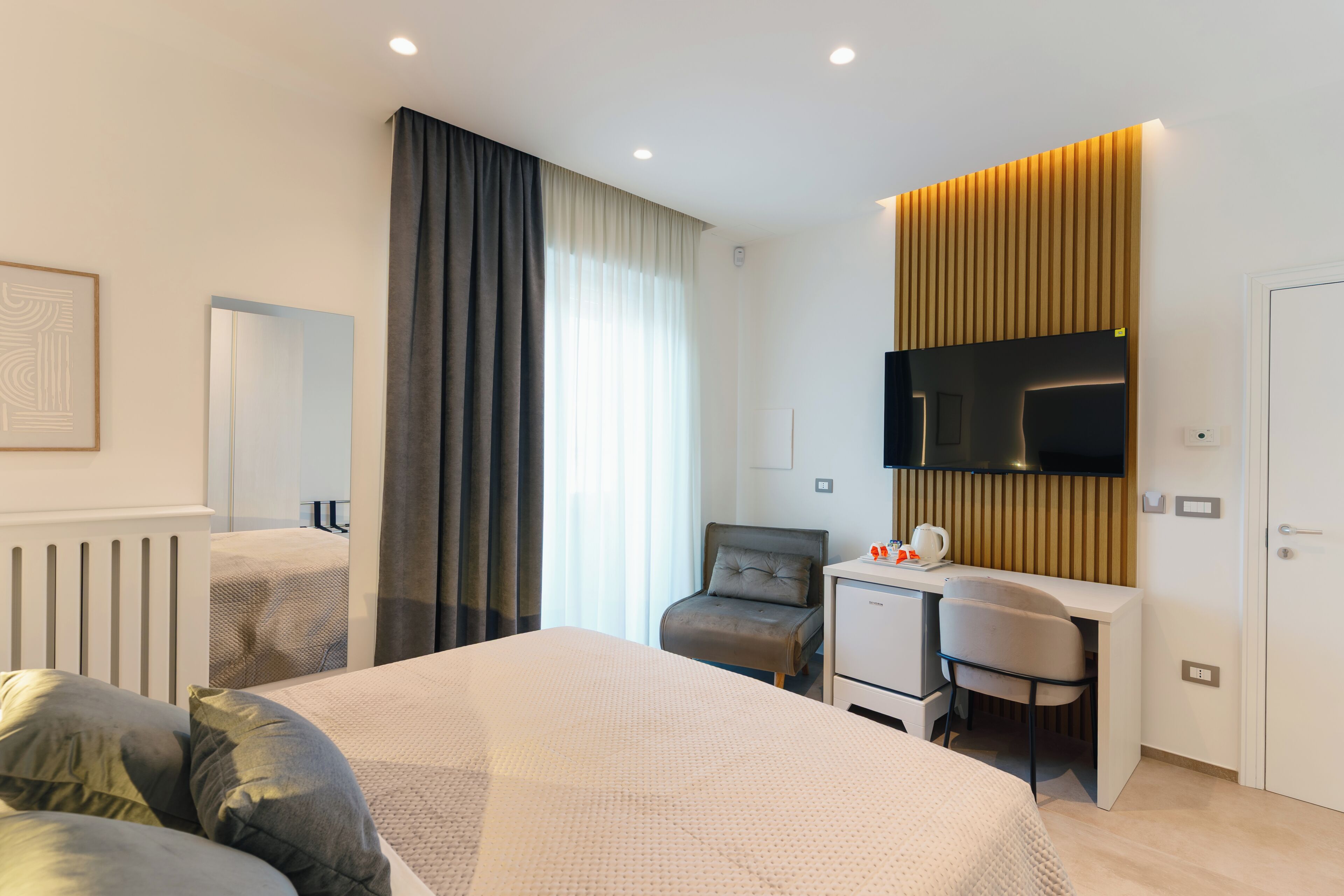 Ein modernes Hotelzimmer mit Bett, Schreibtisch, Sessel, Fernseher und Kleiderschrank.