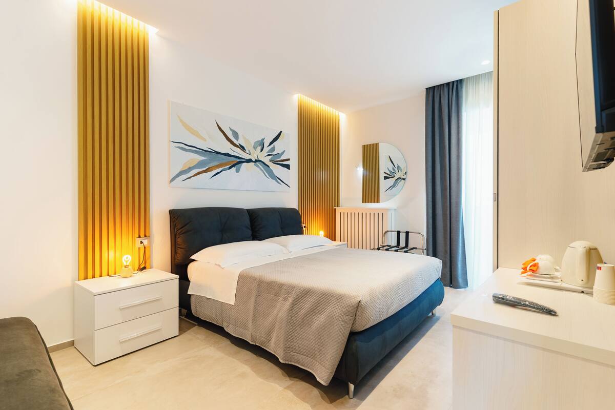 A modern hotel room with a bed, bedside table, and a desk with a remote control.