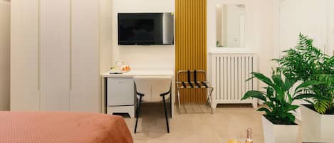 Una habitación de hotel moderna con cama, escritorio, silla, televisión, radiador, plantas en macetas y una botella en la mesita de noche.