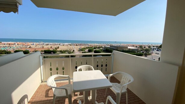 A balcony with a table and chairs, overlooking a beach with umbrellas and people. - Holiday Flat for Families in Bibione (San Michele al Tagliamento)