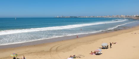 A beach with people sunbathing, umbrellas, and a distant city skyline.