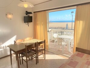 Ein Zimmer mit Esstisch, Stühlen, einem Bett, einem Fernseher und einem Balkon mit Blick auf den Strand.