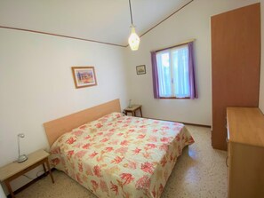 Ein Schlafzimmer mit Bett, Schreibtisch, einem Fenster mit Vorhängen und einem Wandbild.