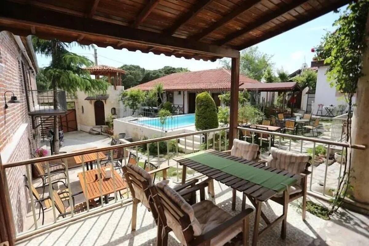 Un patio techado al aire libre con muebles de madera, una piscina y vistas de edificios circundantes.