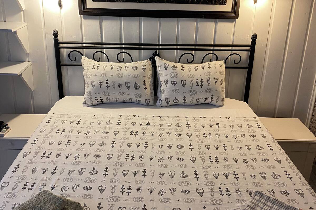 Una cama bien hecha con ropa de cama estampada, cabecera con marco decorativo y lámparas fijadas a la pared.