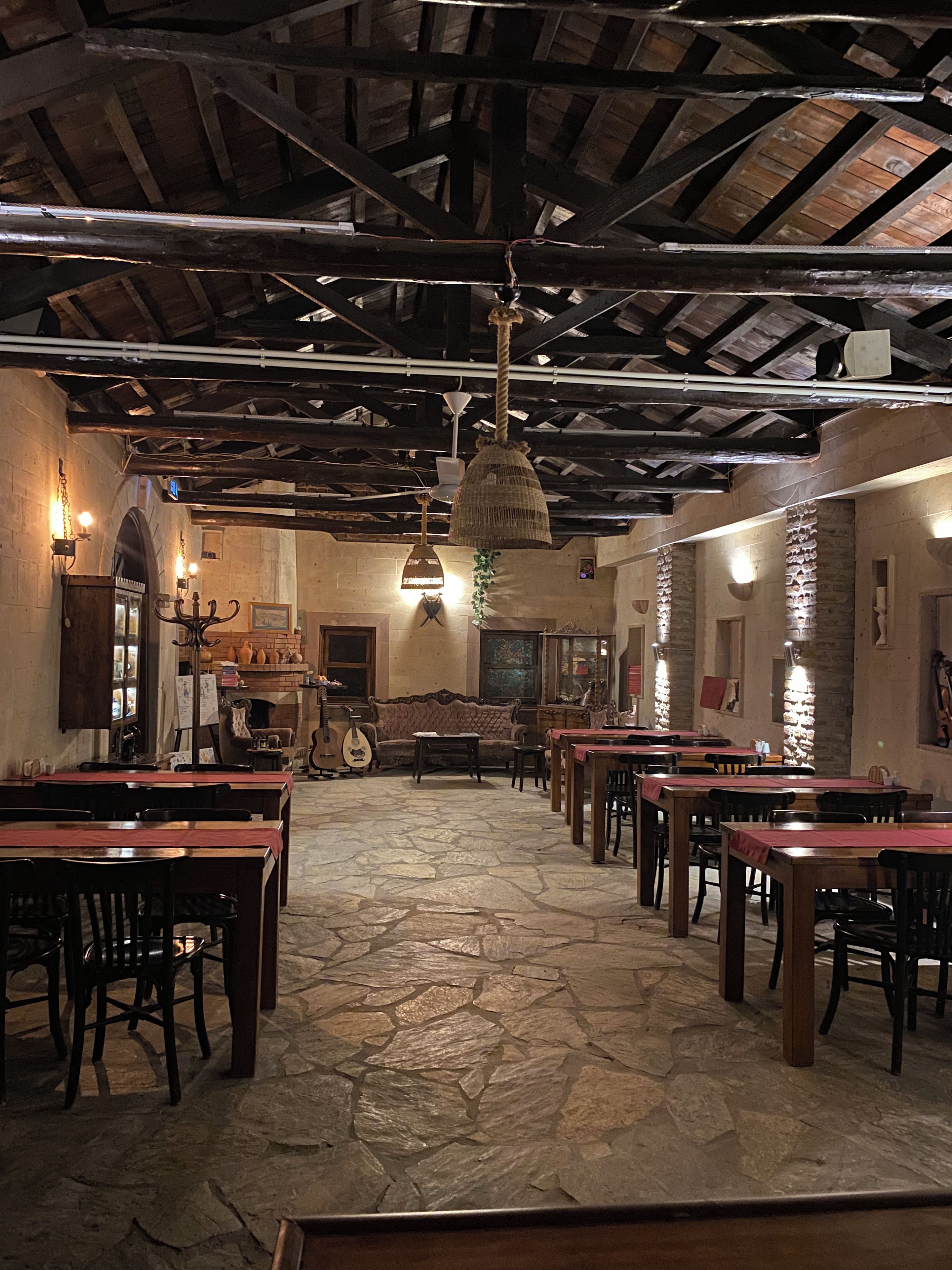 Interior de restaurante com soalho de pedra, mesas e cadeiras de madeira e vigas de madeira expostas no teto.