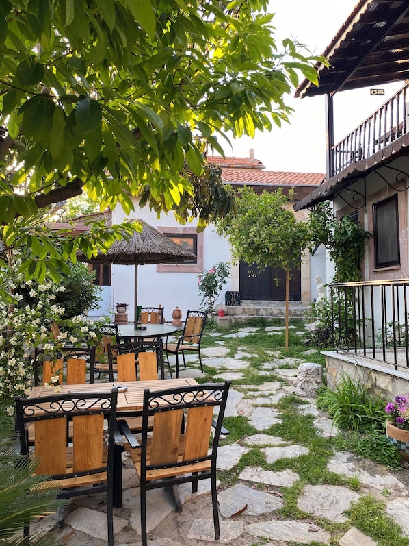 An outdoor patio with stone flooring, wooden tables and chairs, and a thatched umbrella.