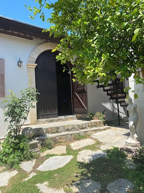 A stone staircase leading to a dark wooden door, a small garden with a statue, and a clear blue sky.
