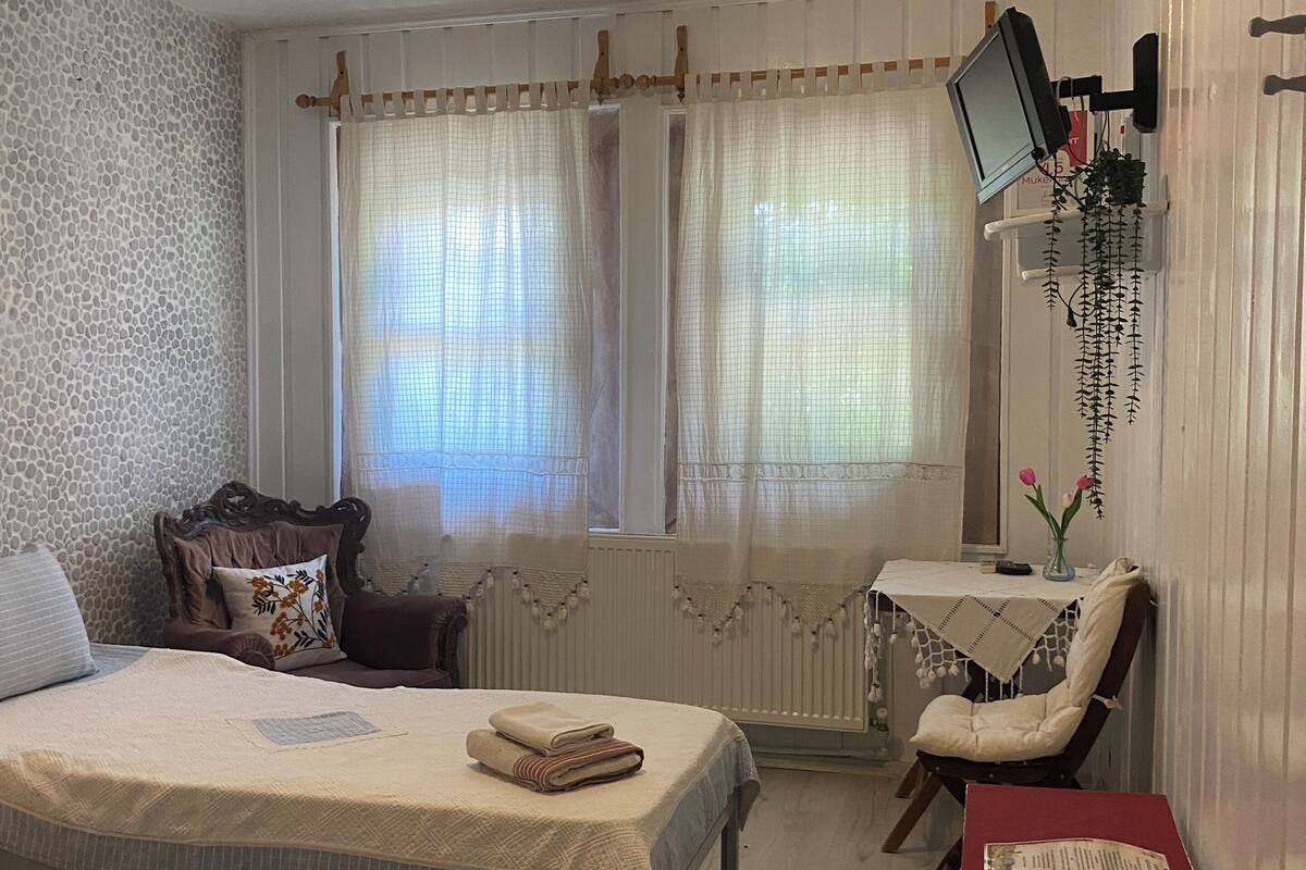 Una habitación con dos camas, un escritorio, una silla, un radiador, un televisor y una mesita con un mantel rojo.