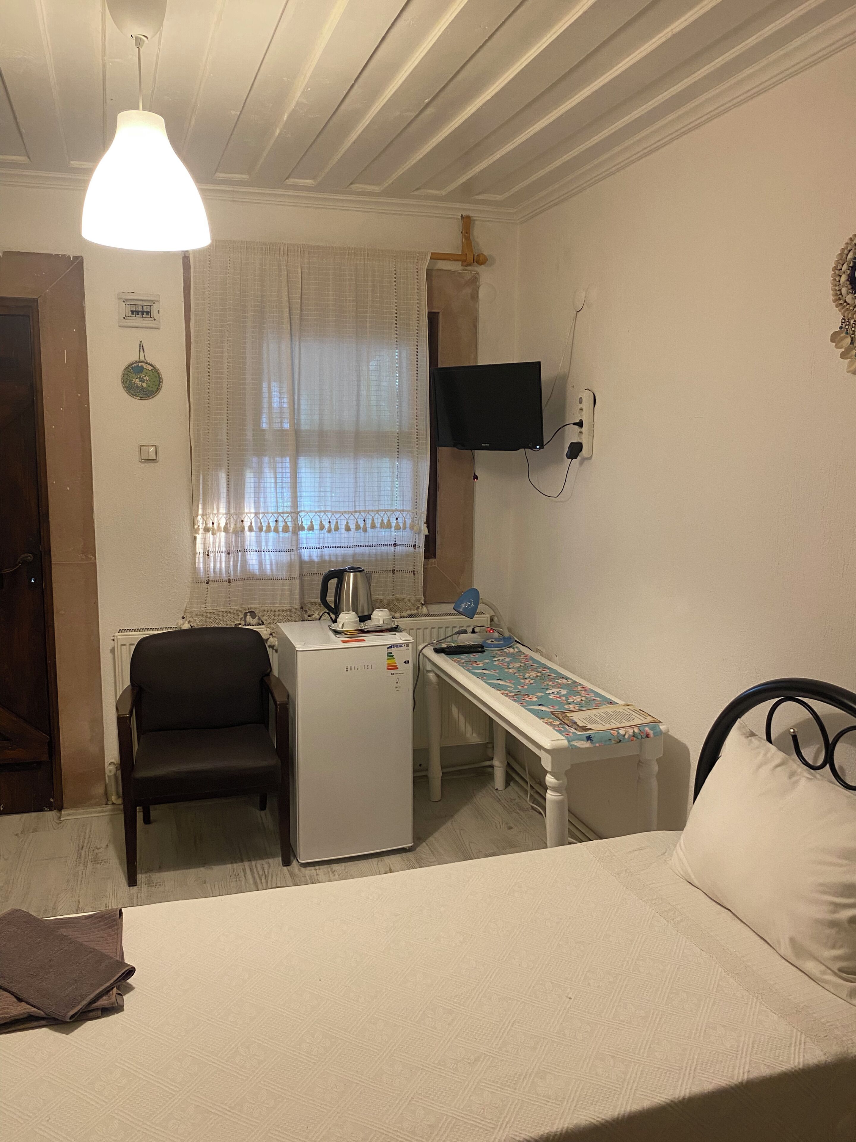 Habitació amb llit, escriptori, cadira, nevera, televisió penjada a la paret i finestra amb cortines.