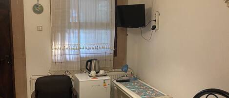 Habitació amb llit, escriptori, cadira, nevera, televisió penjada a la paret i finestra amb cortines.
