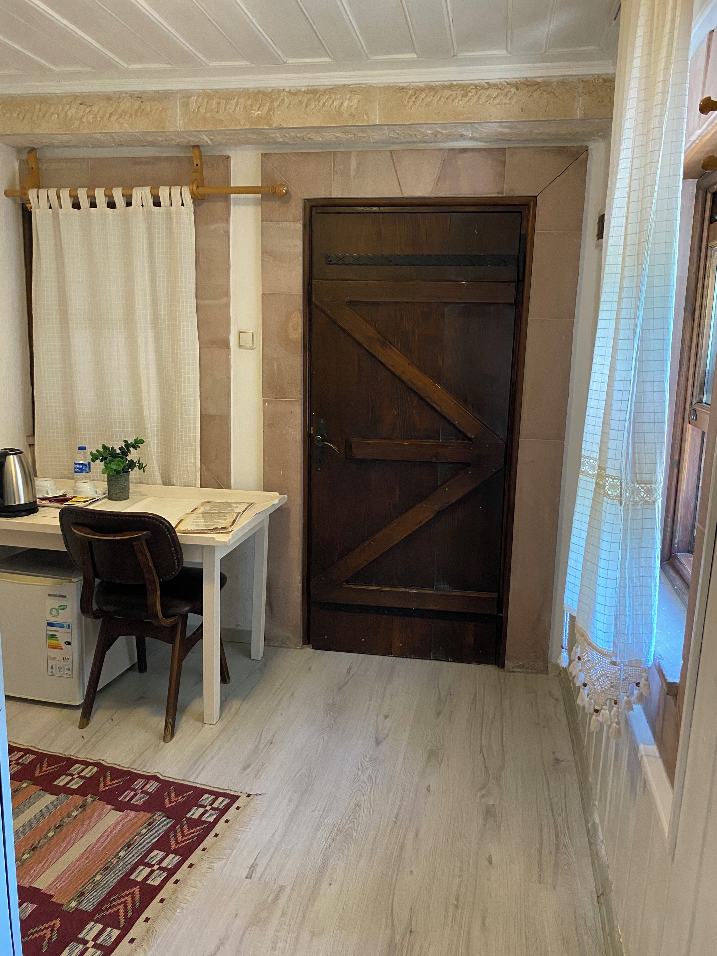 Una stanza compatta con una porta in legno, un tavolino con una sedia, un termosifone e un tappeto decorato.
